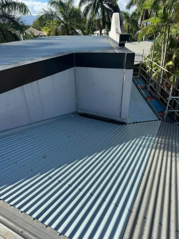 A Rooftop With a Corrugated Metal Surface, a White Wall, and Palm Trees in the Background — HFB Plumbing & Gas in Edmonton, QLD
