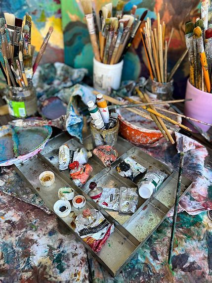 Ein Künstler lächelt, während er einen Pinsel vor mehreren Gemälden hält, die Menschen beim Schwimmen unter Wasser zeigen.