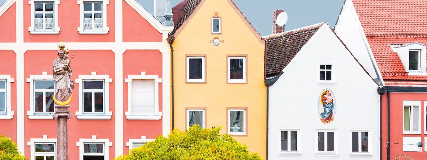 Bunte Häuser im europäischen Stil mit Giebeldächern stehen in einer Reihe, im Vordergrund ist eine Statue zu sehen.
