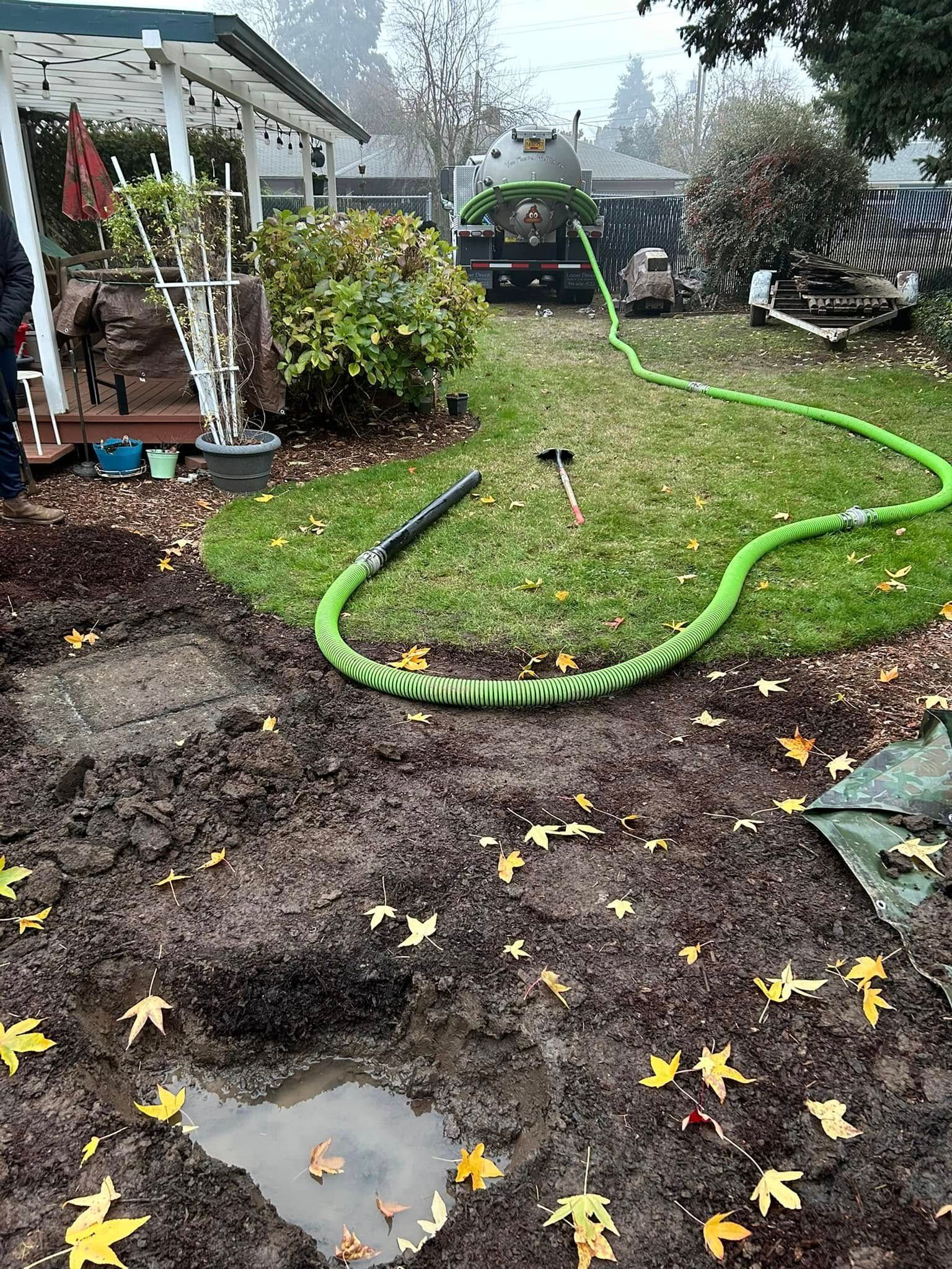 A green hose is sitting in the middle of a muddy yard.