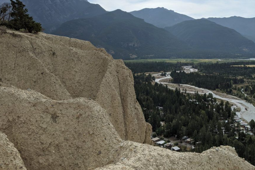 Rocky cliff overlooking a forested river valley and distant mountains under a cloudy sky