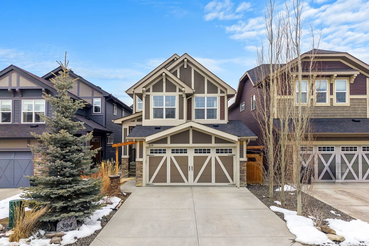 Row of suburban townhouses with a central tan house, driveway, and patches of snow on the ground