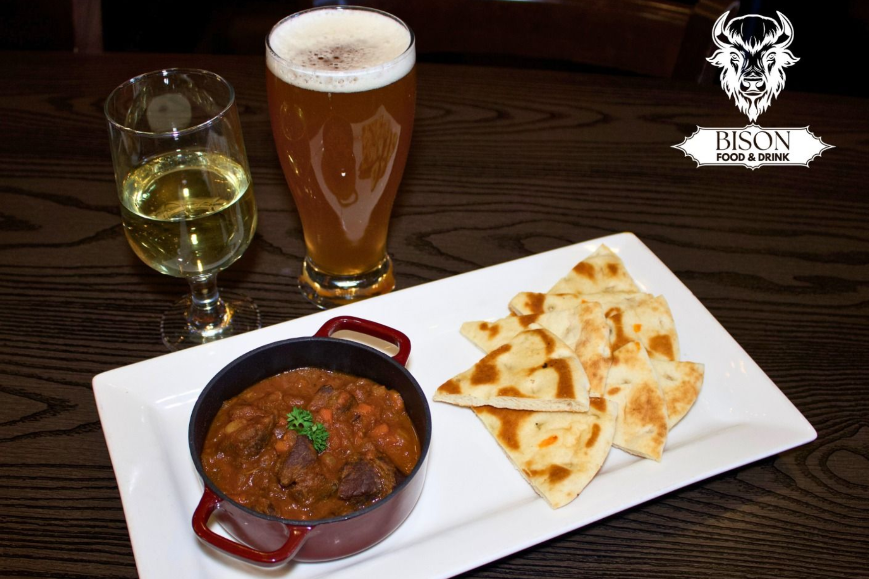 Beer, white wine, and a red curry with naan on a table