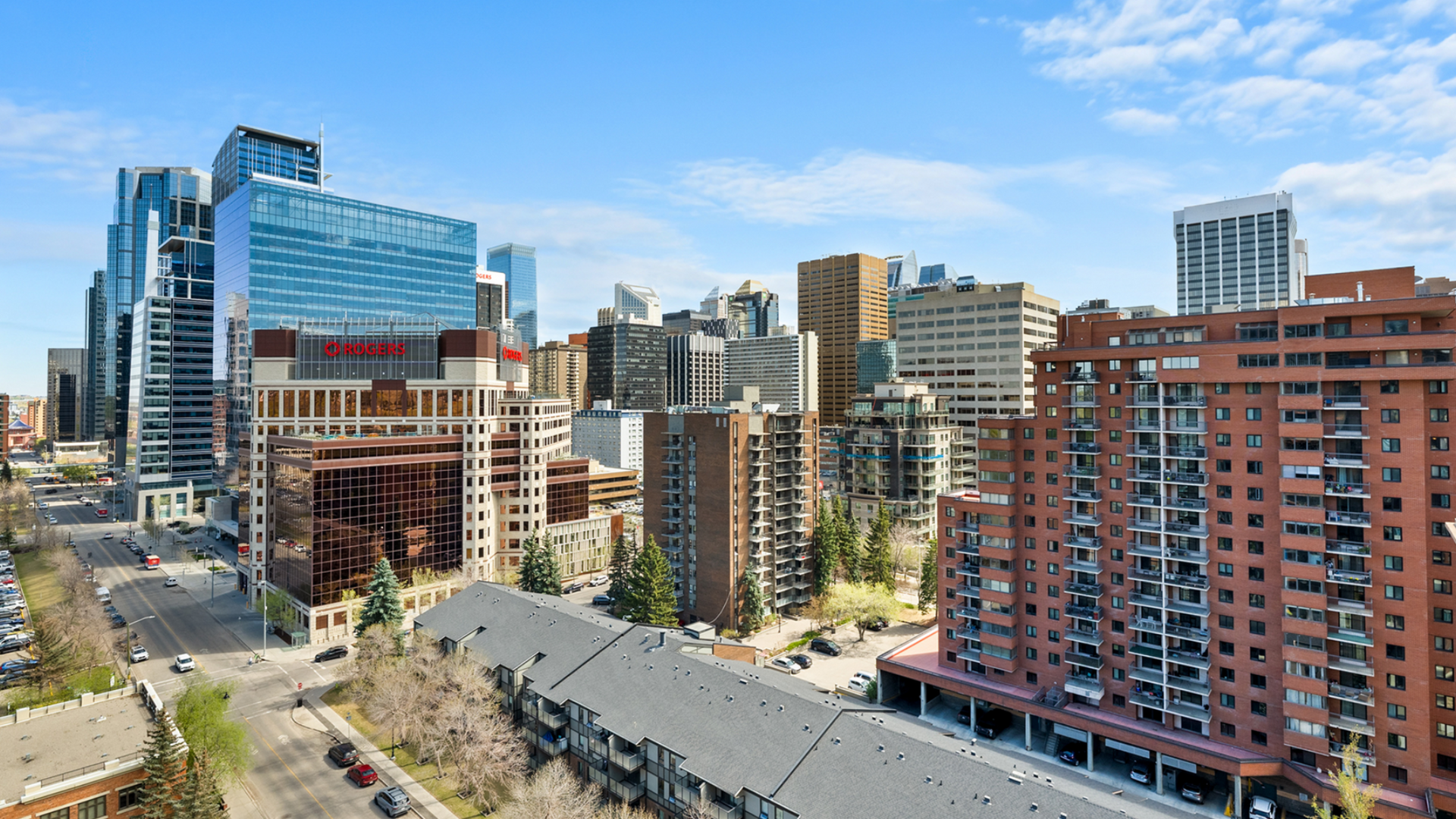 A view of a sunny city skyline featuring modern skyscrapers, brick high-rise buildings, and a street below.