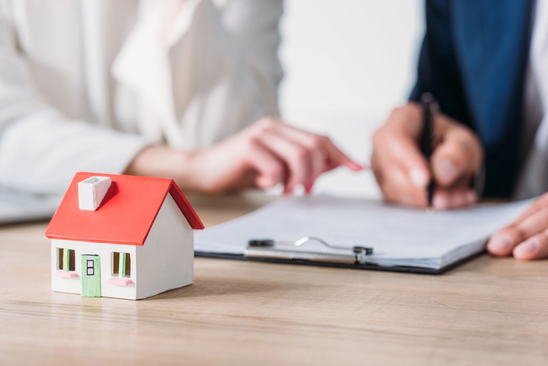 Two people are sitting at a table with a model house and a clipboard.