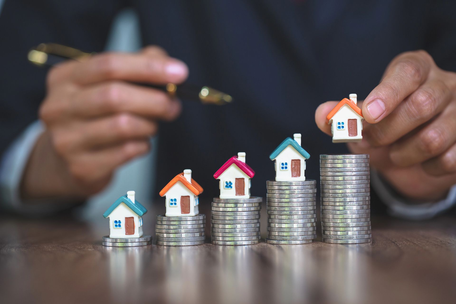 A man is stacking small houses on top of coins.