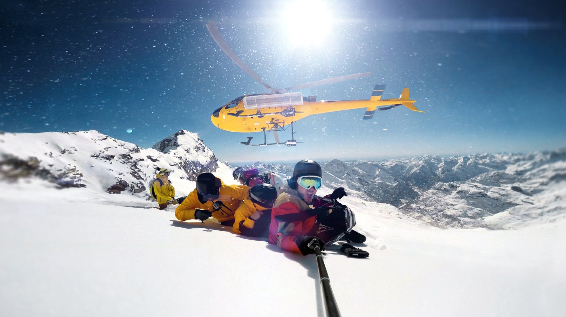 A group of people are sitting on top of a snow covered mountain while a helicopter flies overhead.