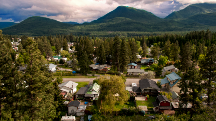 Small town neighborhood with colorful houses below forested mountains under a cloudy sky
