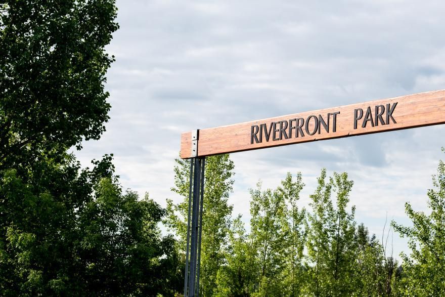 Sign reading “Riverfront Park” above green trees under a cloudy sky