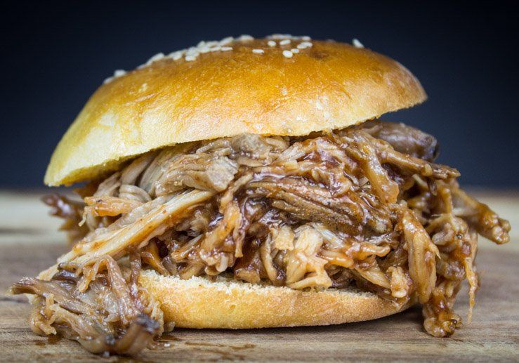 A pulled pork sandwich on a bun with sesame seeds on a wooden table.