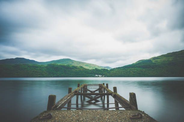 There is a dock in the middle of a lake with mountains in the background.
