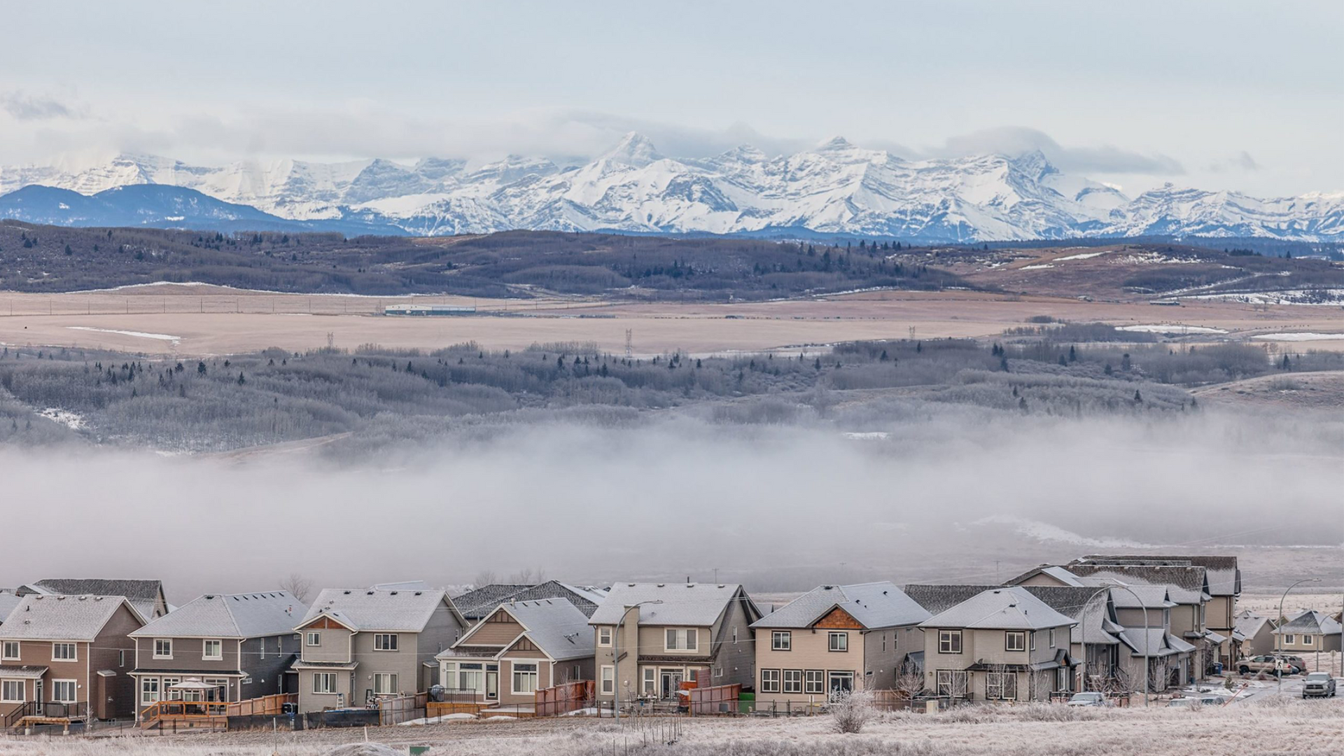 A row of houses sits in front of a fog-covered valley with snow-capped mountains in the background.