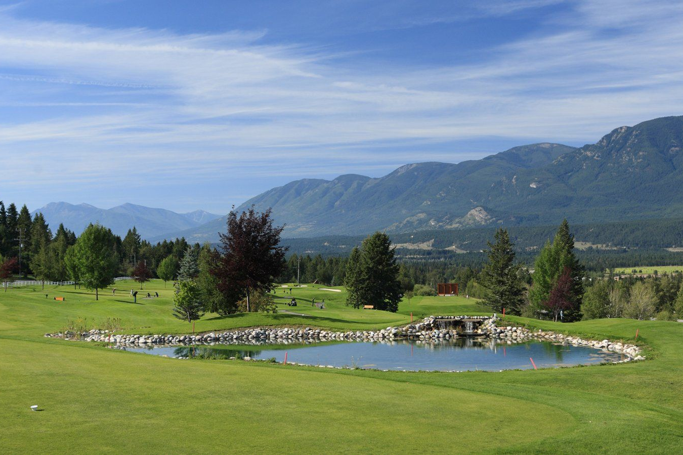 Green golf course with a small pond and mountains under a blue sky