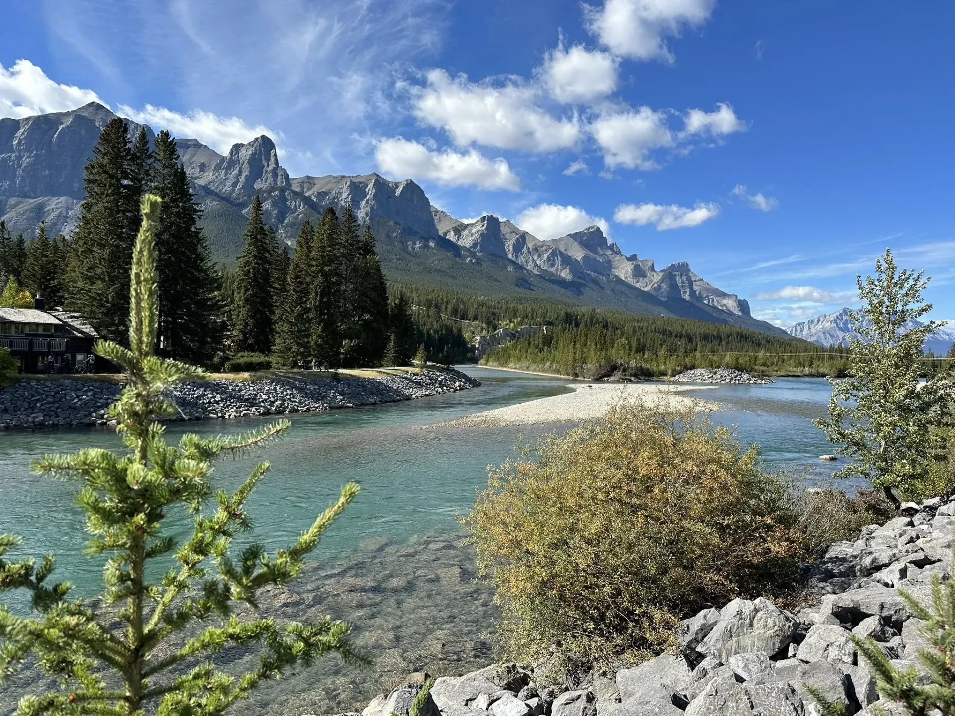 Clear river flows through rocky terrain, mountains in the distance under a blue sky.
