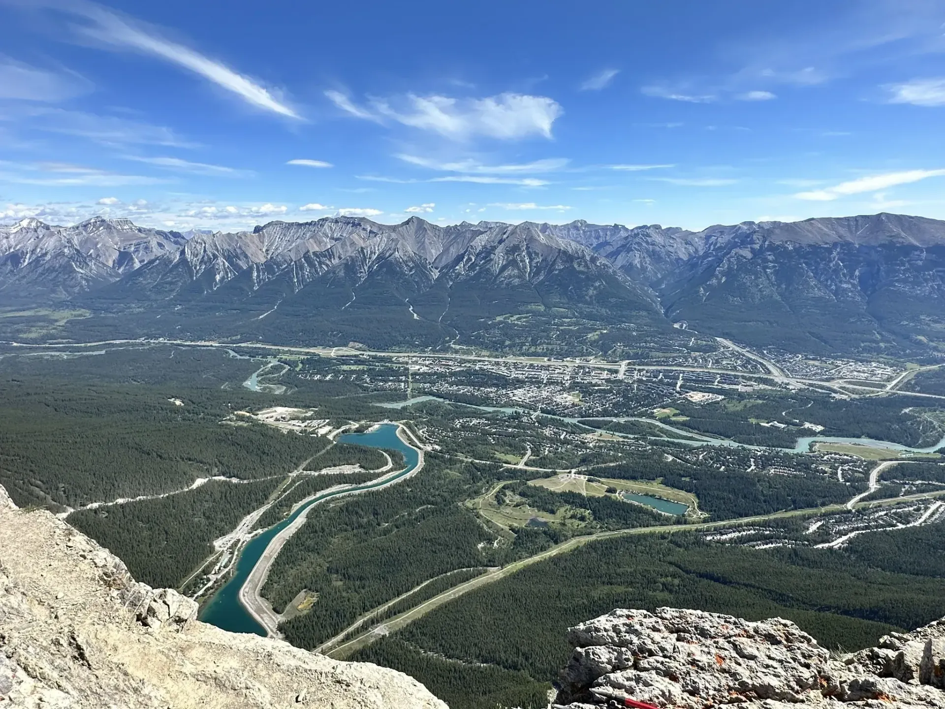 Scenic mountain vista with a city nestled in a valley, and a river winding through forests. Clear blue sky.