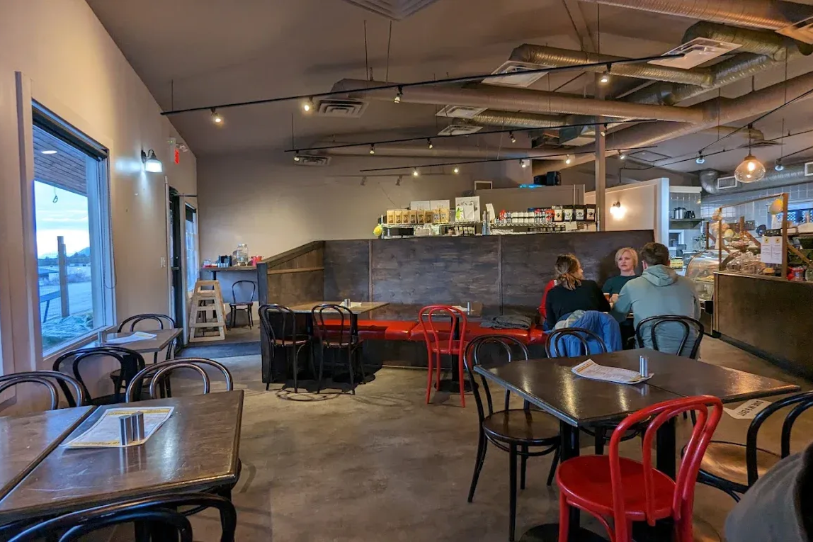 Cozy café interior with red and black chairs, wooden tables, and two people seated near the back.