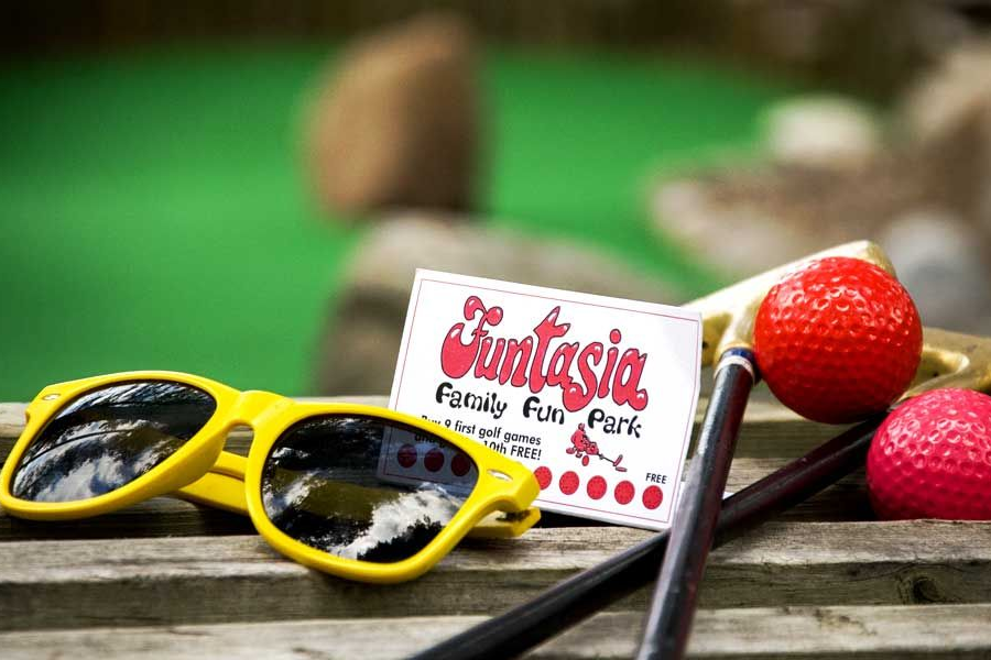 Yellow sunglasses beside strawberries and a cherry box on a wooden surface.