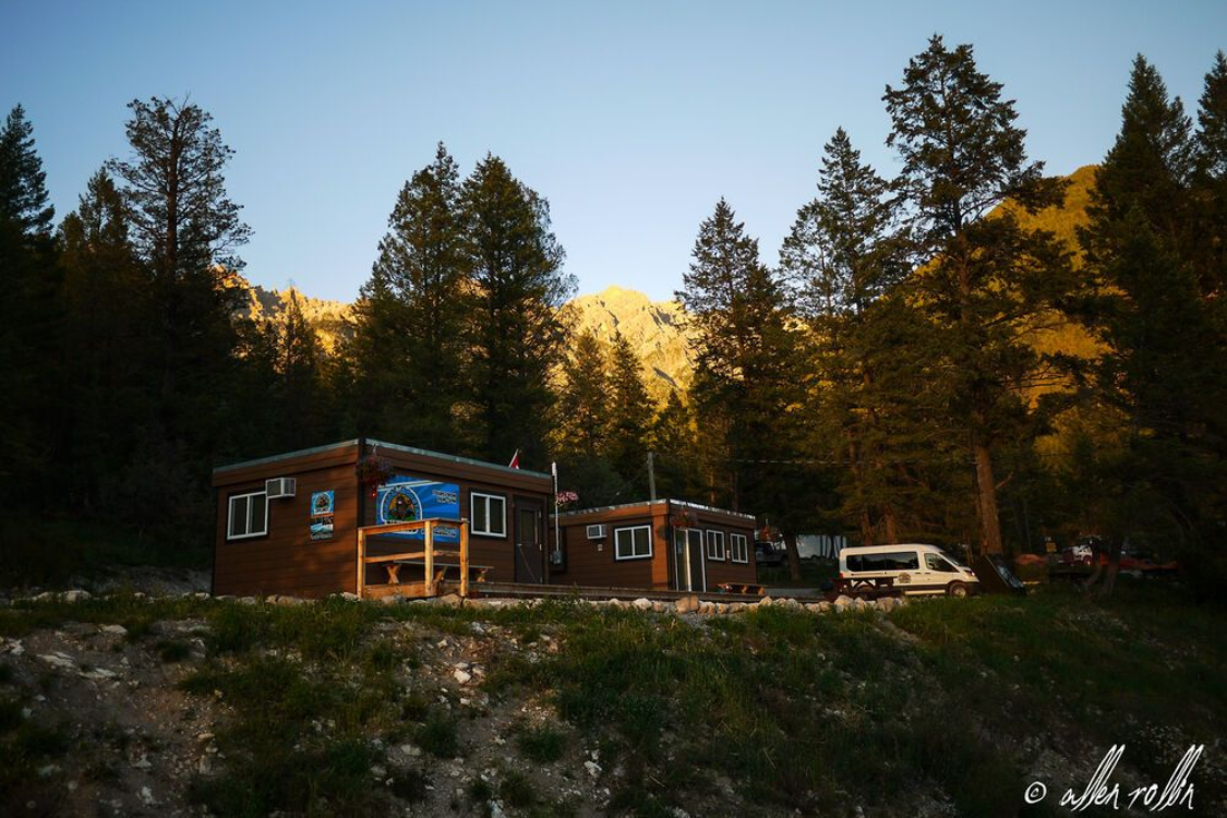 Rustic cabin at sunset in a forest, with parked van and tall pine trees around it