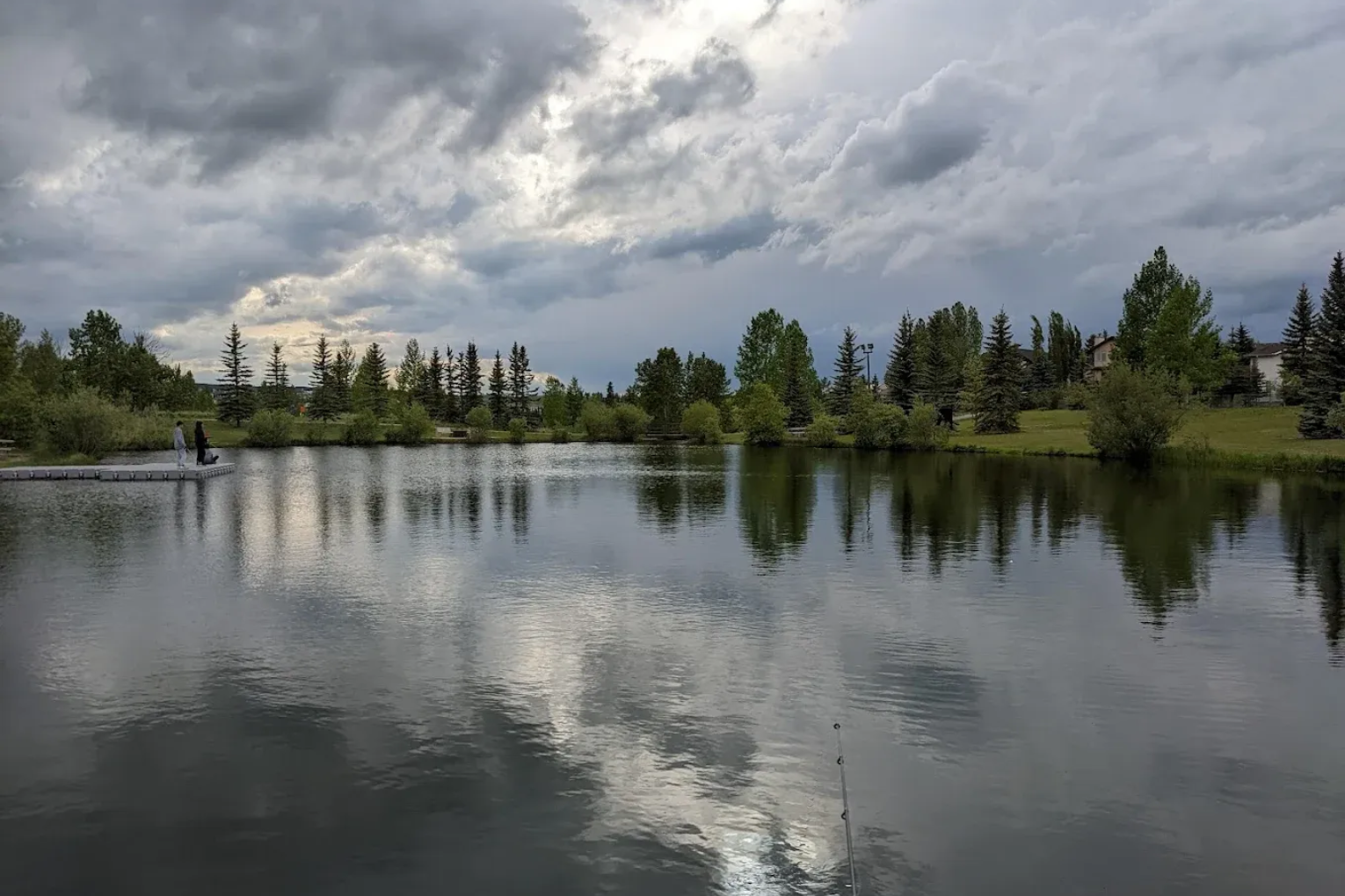 Calm lake reflecting cloudy sky and pine trees along the shore