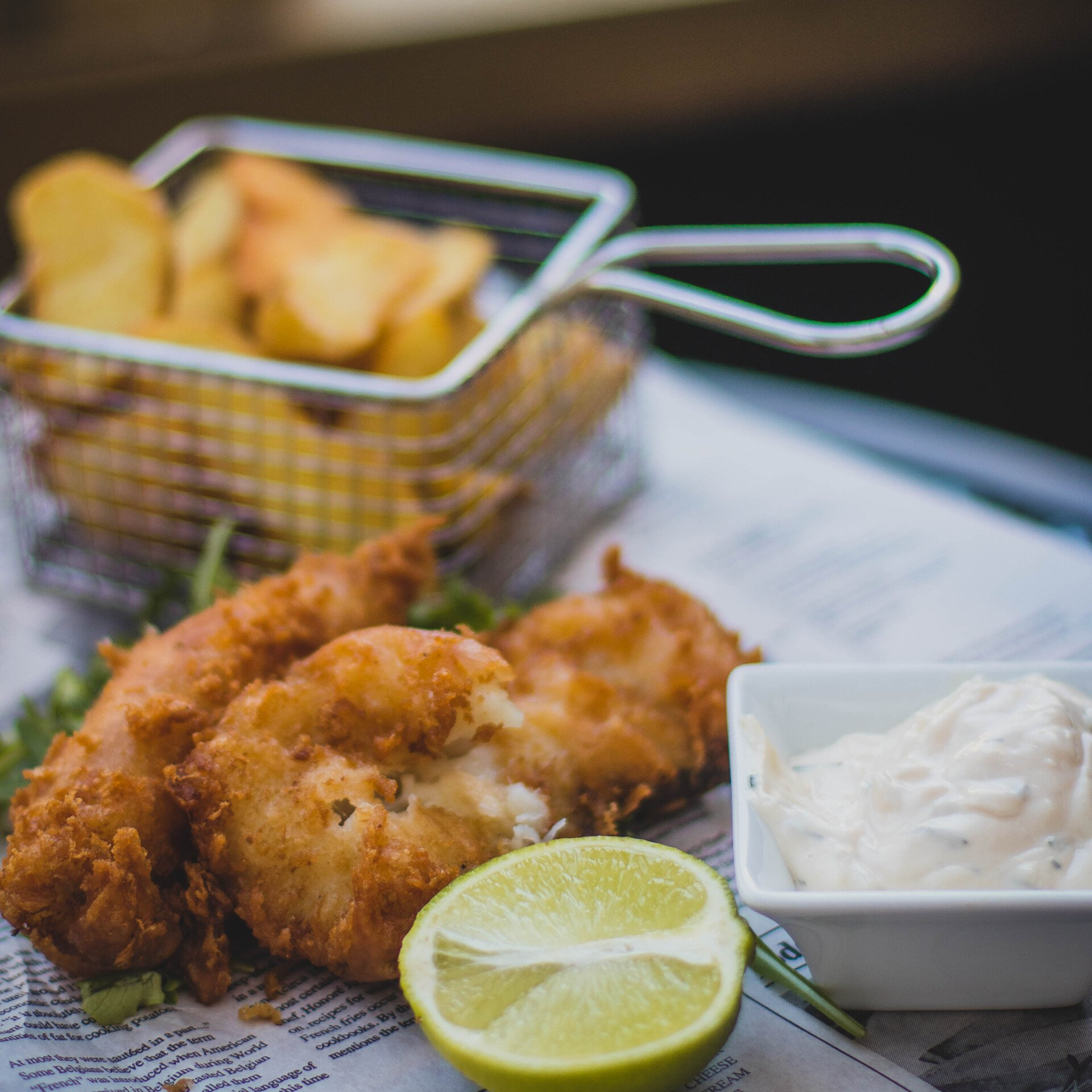 A plate of food with a basket of chips and a bowl of sauce on a table.