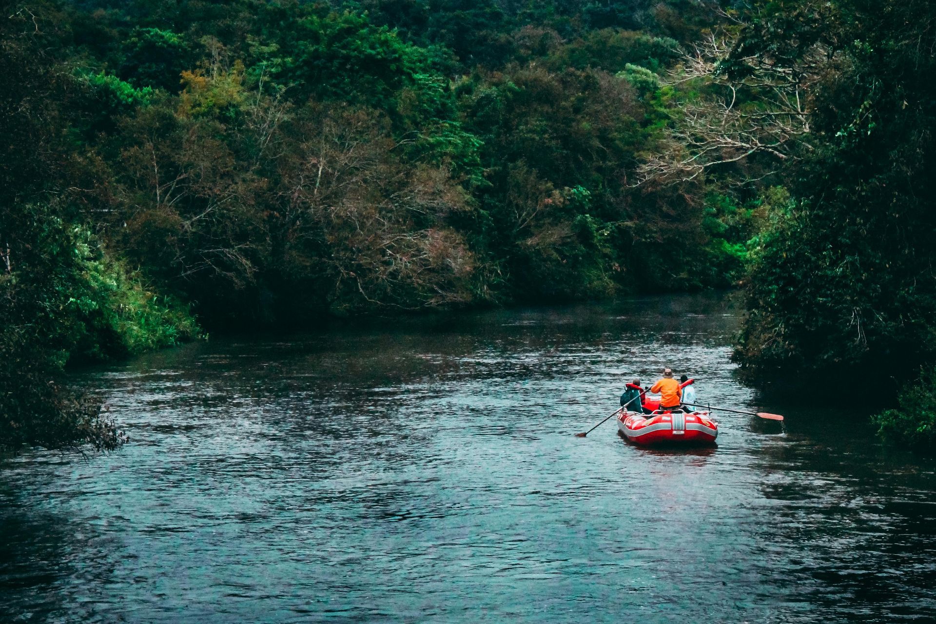 Red raft floating calmly down a river surrounded by forested mountain scenery.