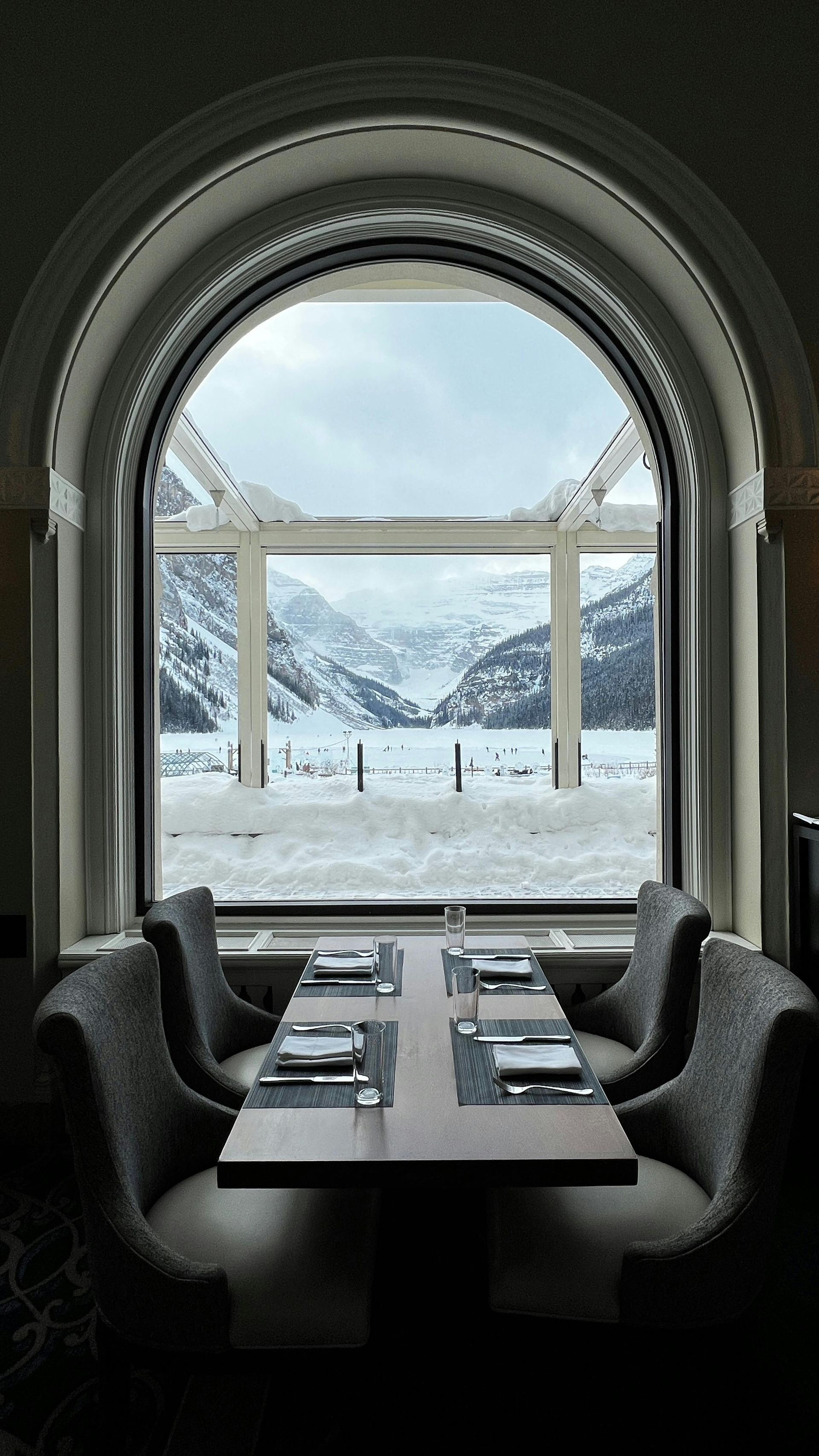 Restaurant table set for dining, framed by a large arched window with snowy mountain view.