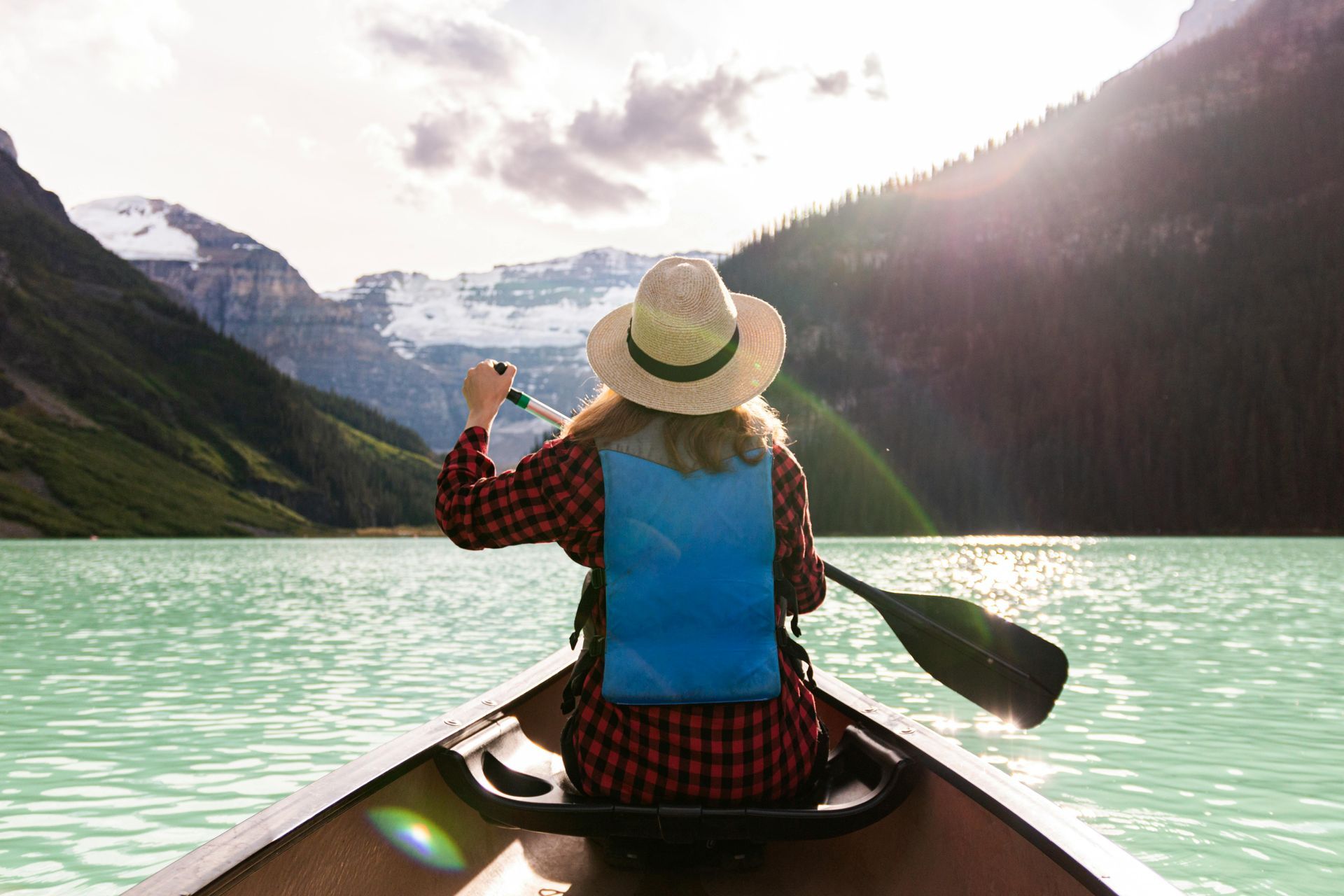 Person paddling a canoe on calm waters with mountains in the background