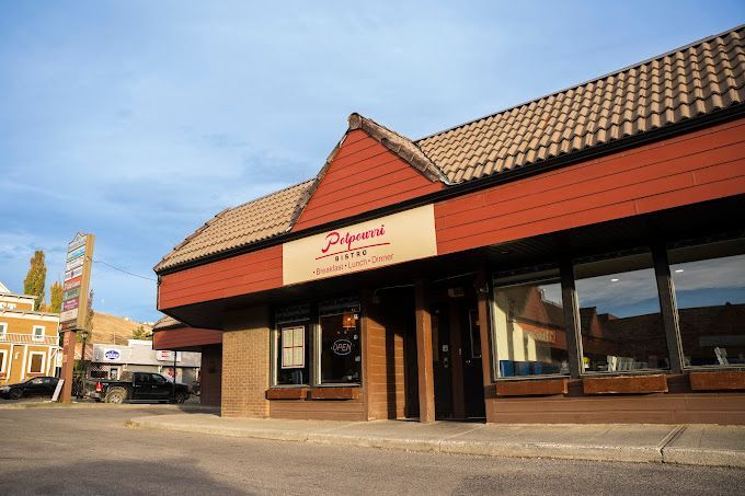 Exterior of a brick storefront with red awnings and large windows on a sunny street