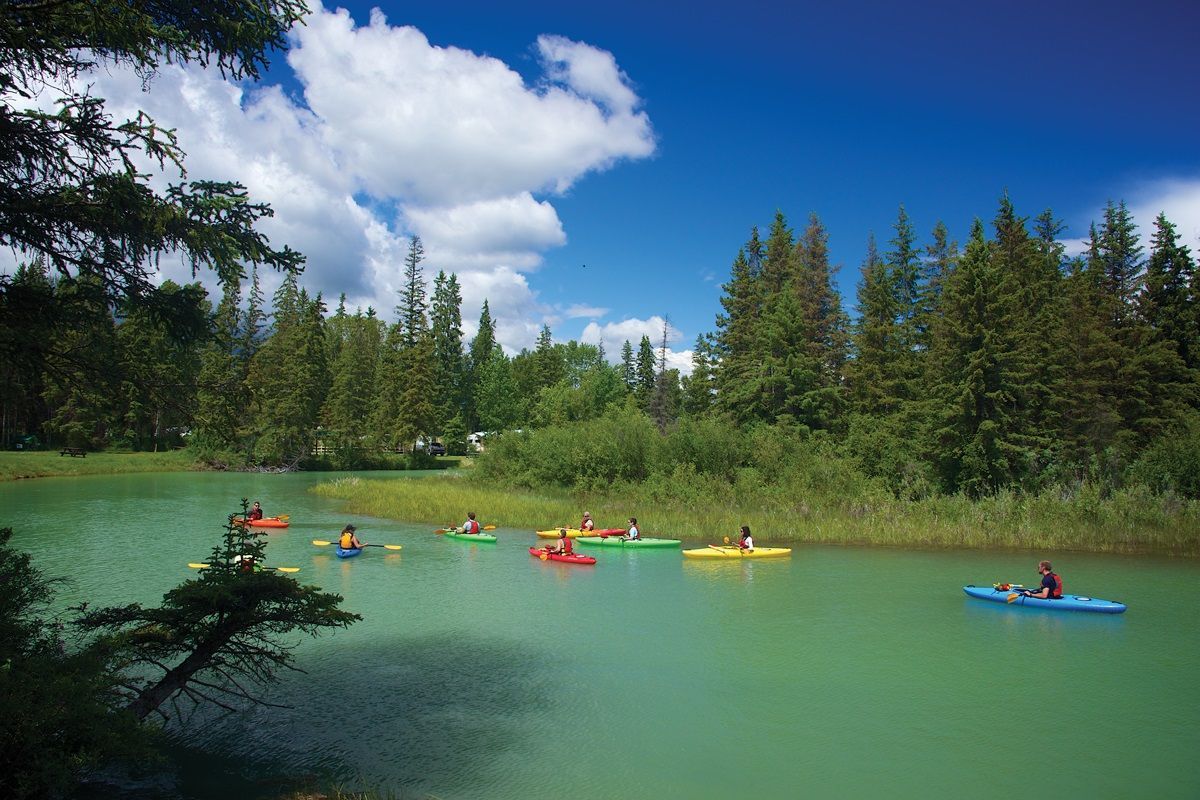 People kayaking on a turquoise lake surrounded by evergreen forest under a blue sky