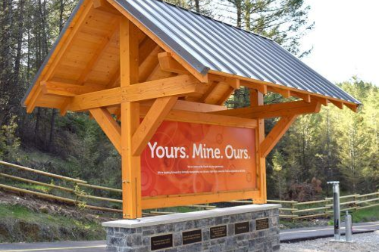 Wooden roadside sign under a metal roof reading “Yours. Mine. Ours.”