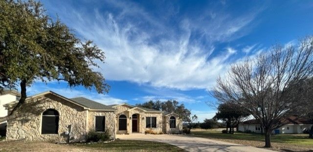 A house with a tree in front of it and a blue sky with clouds.