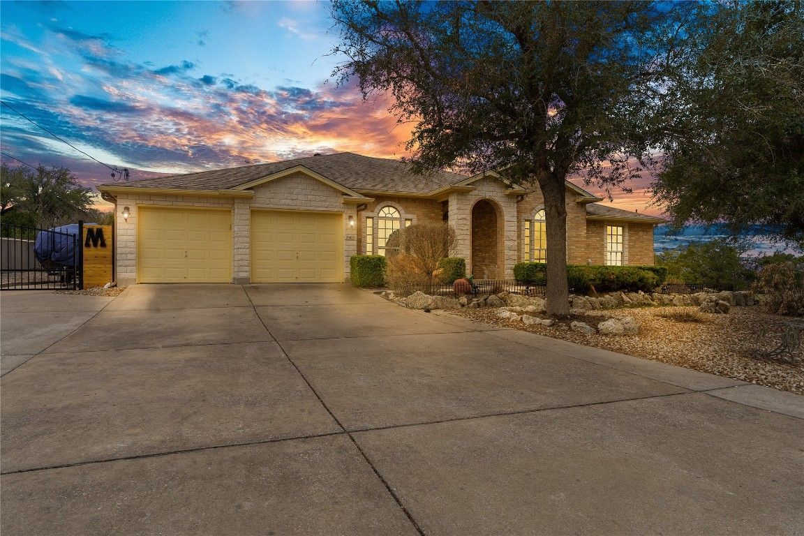 A large house with a large driveway and a sunset in the background.