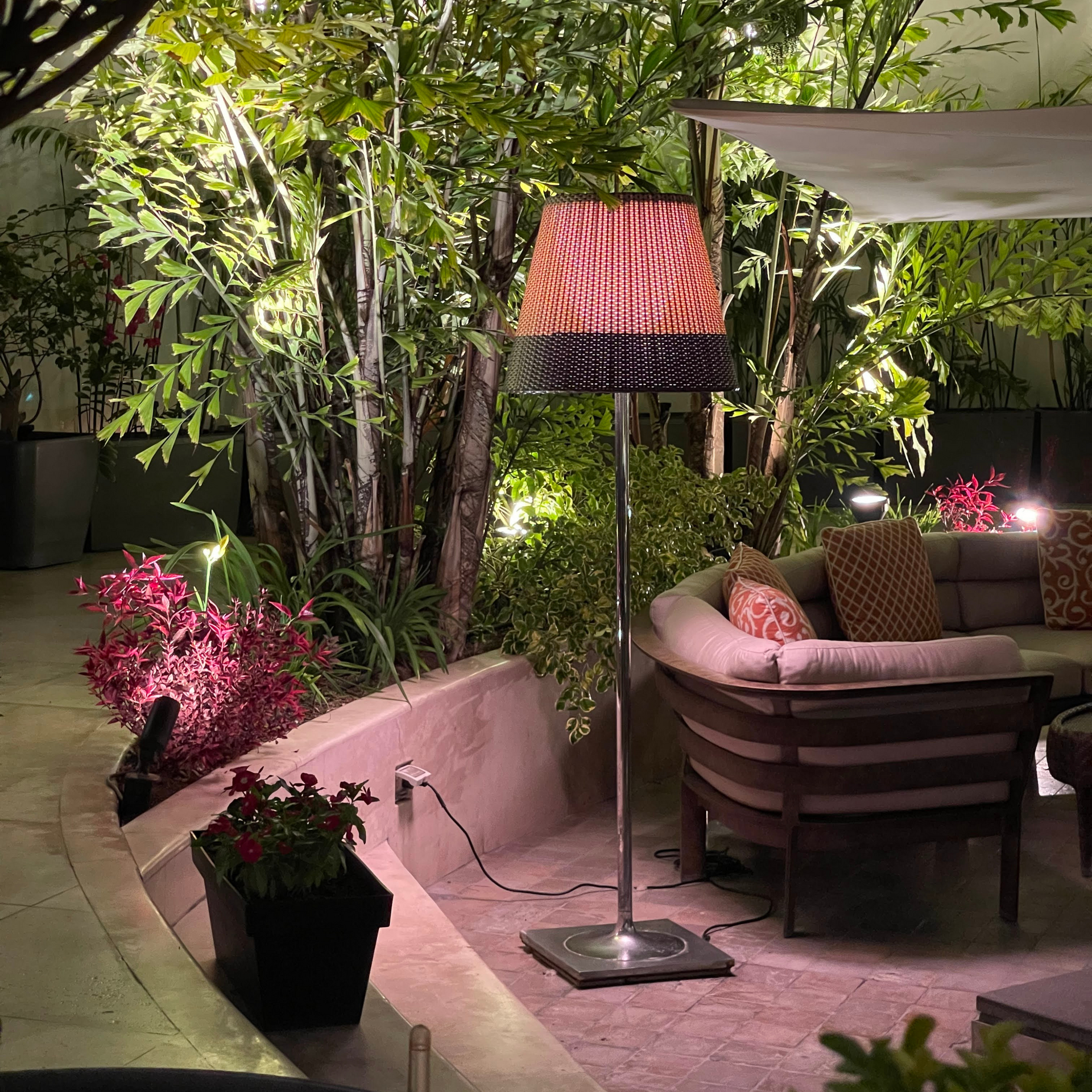 Una lámpara con pantalla roja está colocada en un patio junto a un sofá.