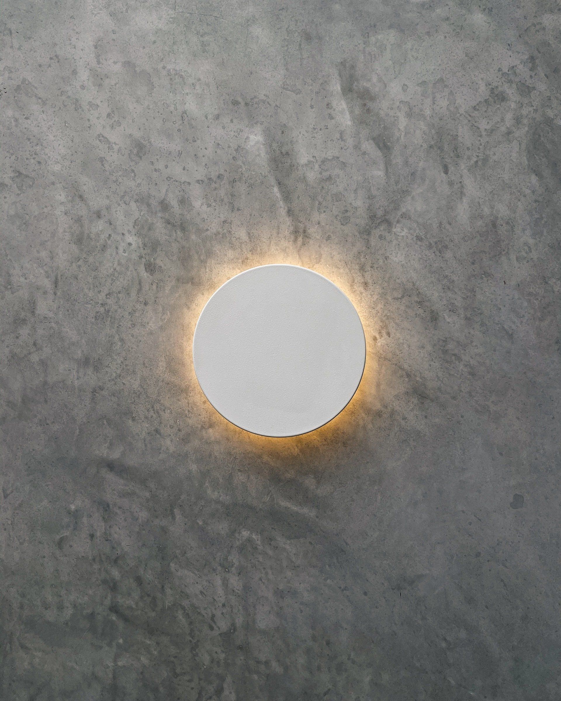 Un círculo blanco con una luz dentro está sobre una pared de hormigón.