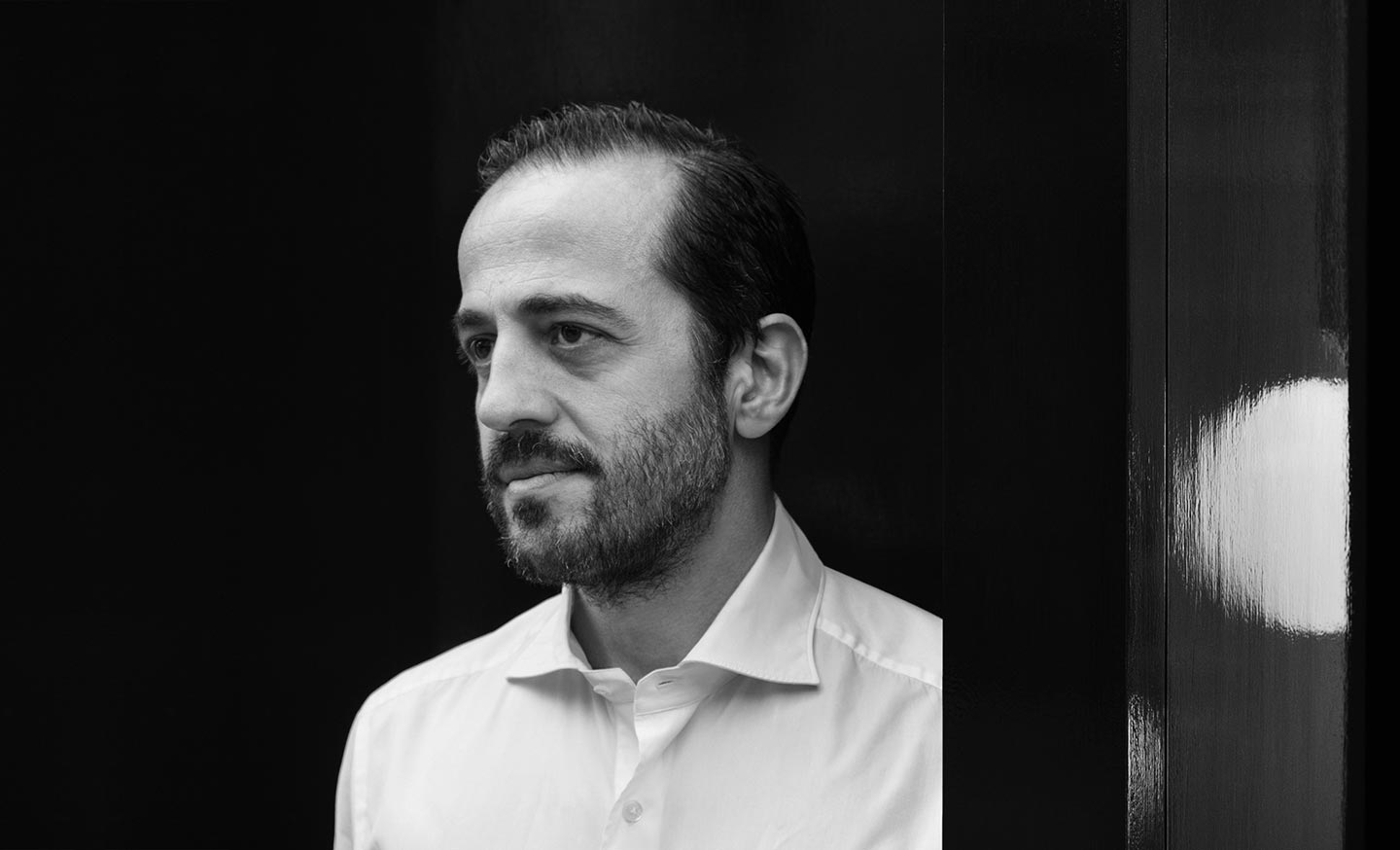 Una fotografía en blanco y negro de un hombre con barba que lleva una camisa blanca.