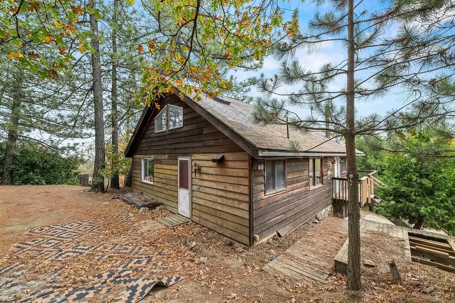 Rustic wooden cabin in a wooded area with autumn leaves and trees surrounding it