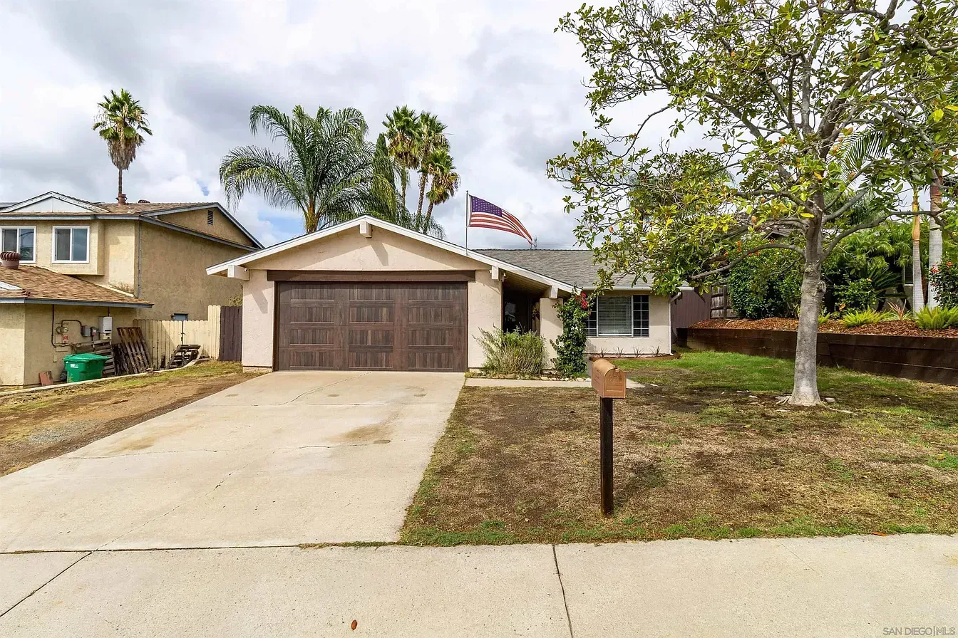 Suburban house with a two-car garage, driveway, front lawn, and an American flag by the entrance