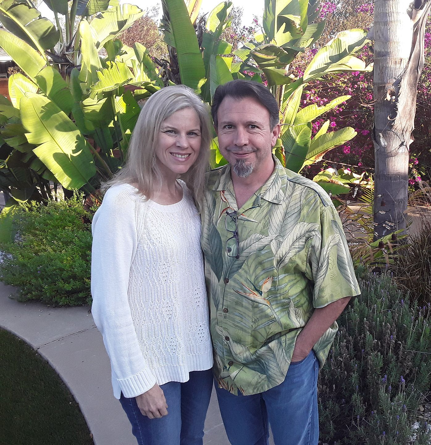 Two people standing together in a lush garden, smiling in front of tropical plants.