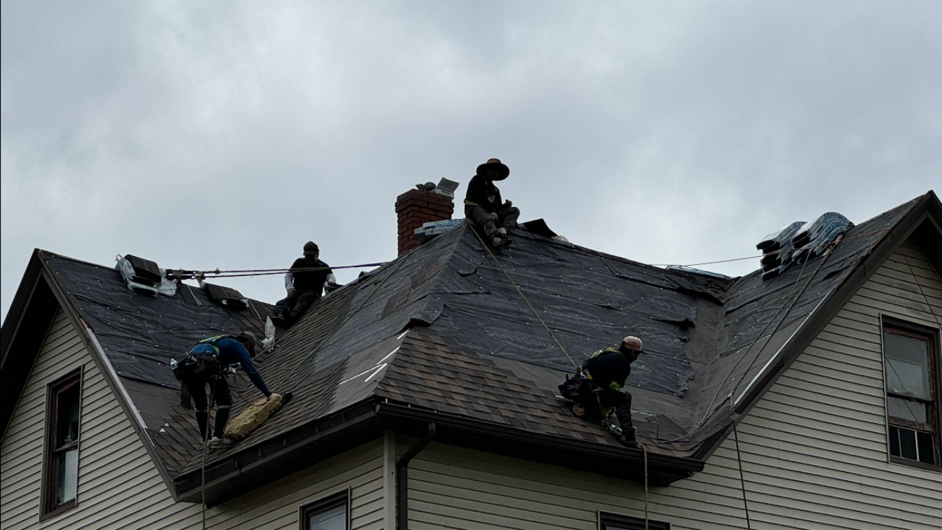Roofers working on a house roof under an overcast sky.