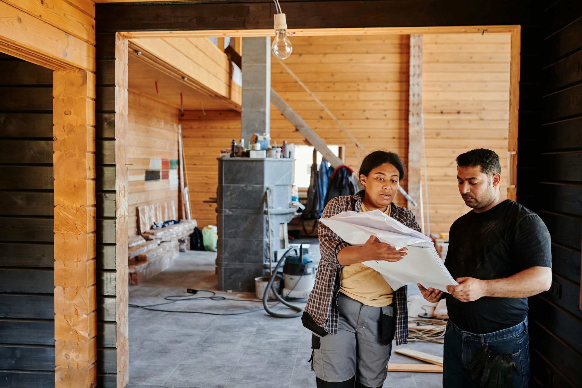 Two people reviewing blueprints inside a wood-paneled building under construction.