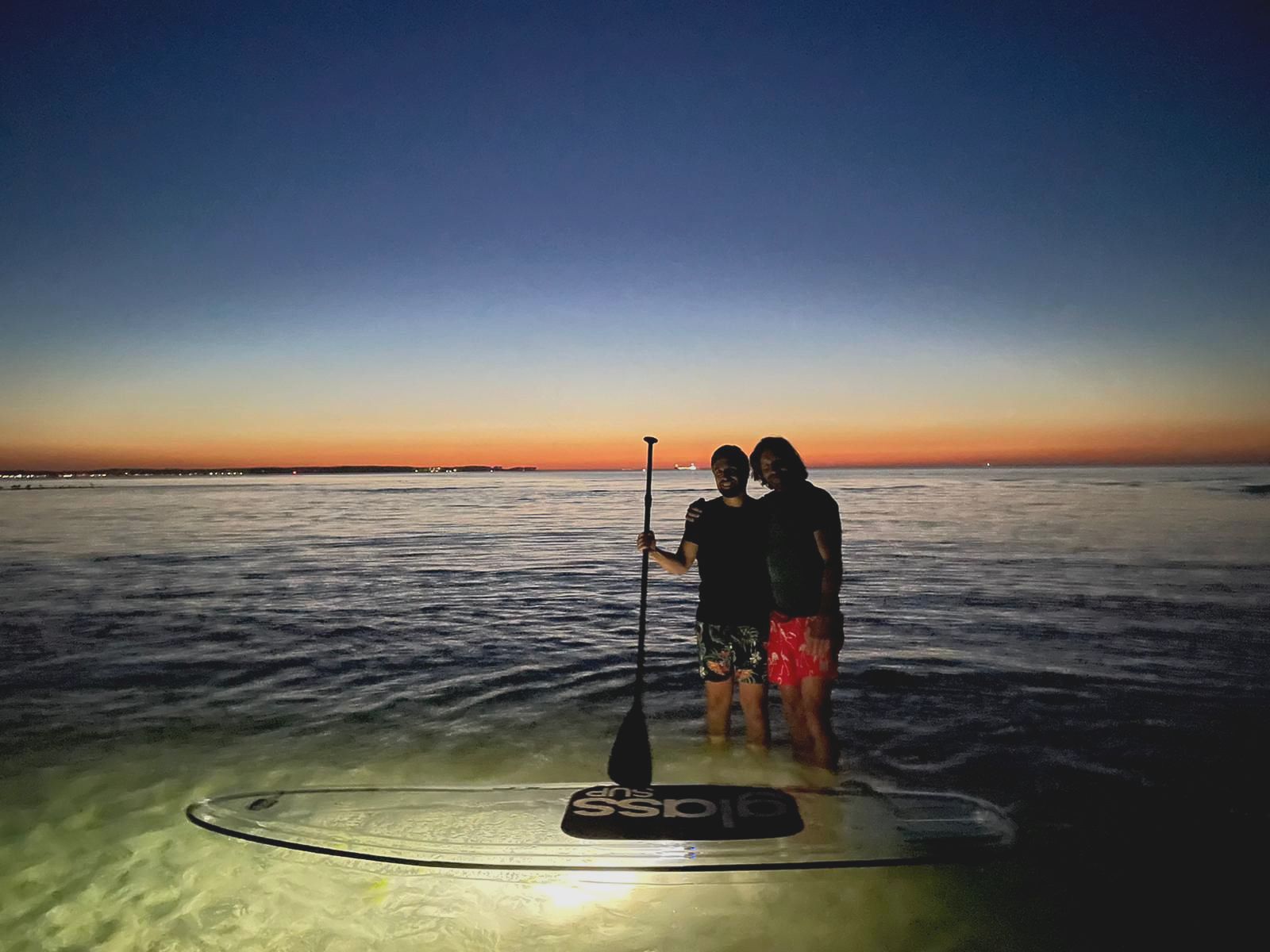 Zwei Personen stehen bei Sonnenuntergang auf einem glassSUP im Meer.