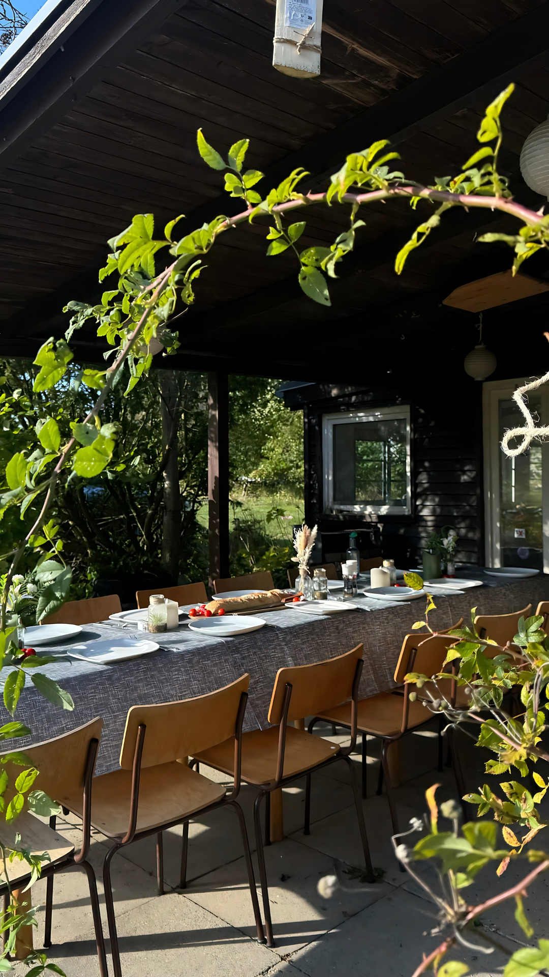 Eine Terrasse mit einem langen Tisch und Stühlen unter einem Baldachin.
