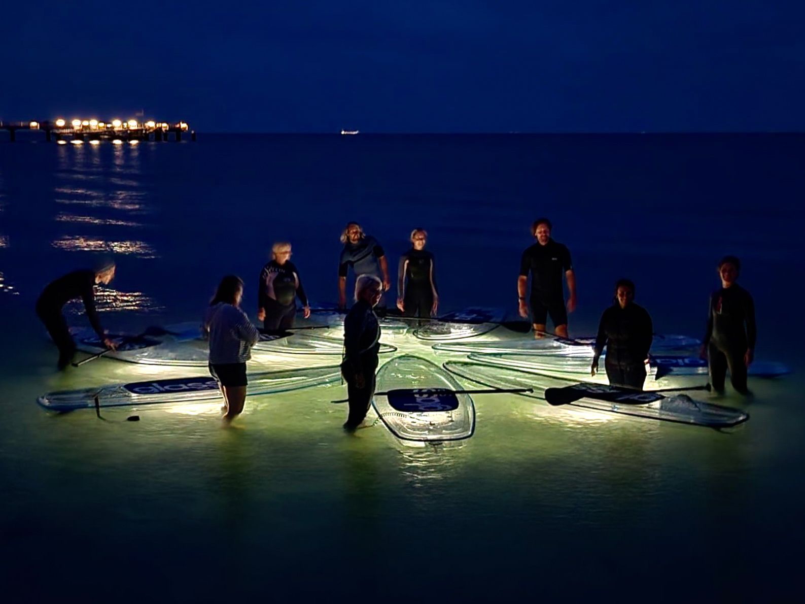 Eine Gruppe von Menschen stehen nachts sternförmig mit den glassSUP Boards im Meer.