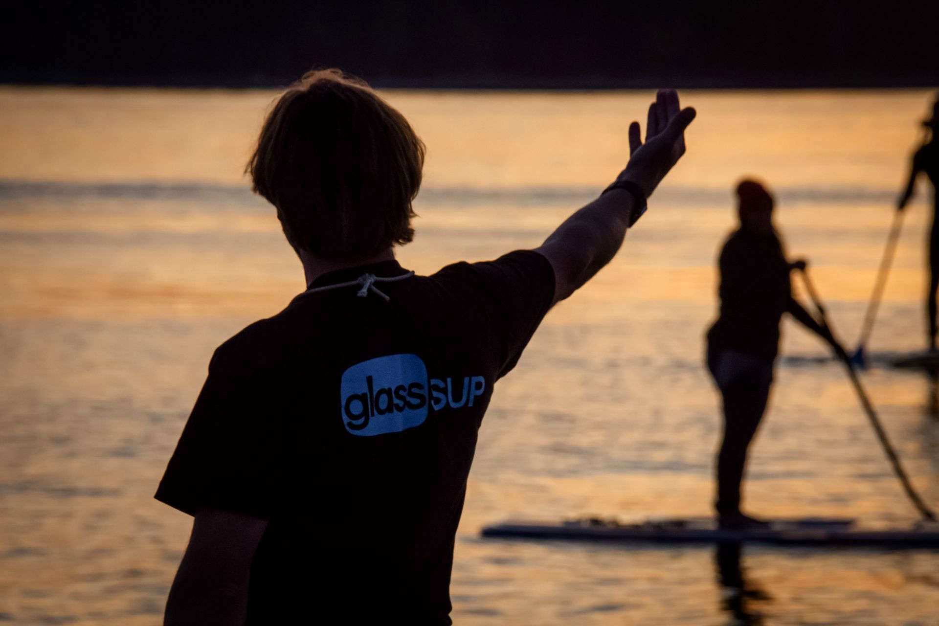 Ein Mann in einem glassSUP-Shirt steht im Wasser und winkt