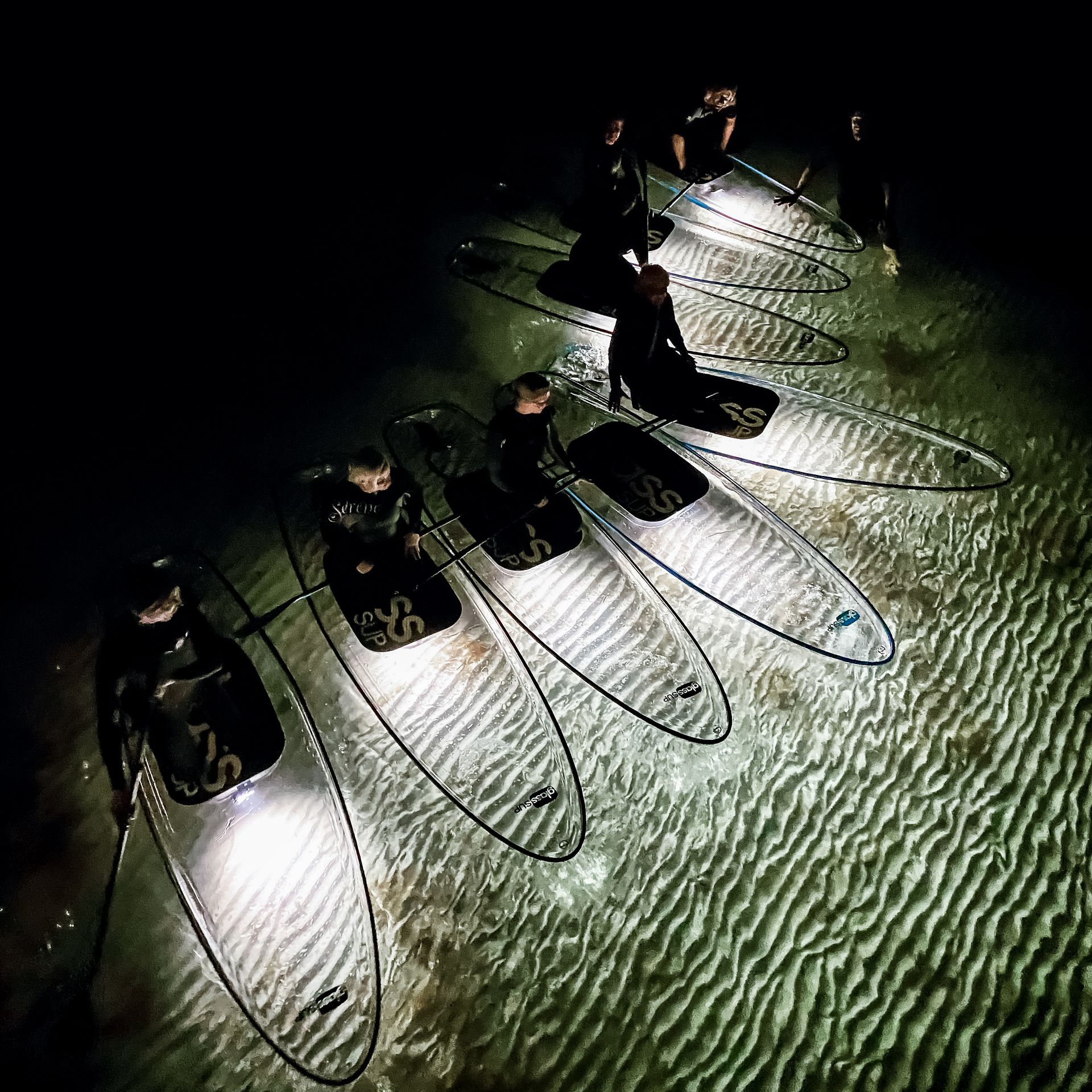 Eine Gruppe von Menschen sitzt nachts auf beleuchteten glassSUPSs im Wasser