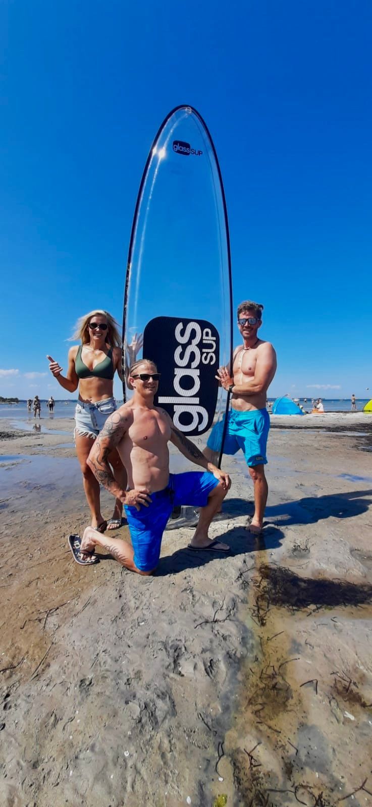 Eine Gruppe von Menschen steht mit einem glassSUP in der Hand an einem Strand.