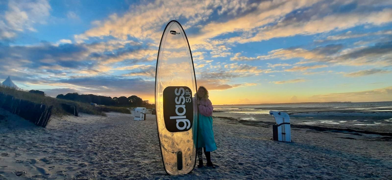 Zwei Personen stehen bei Sonnenuntergang neben einem glassSUP an einem Strand.
