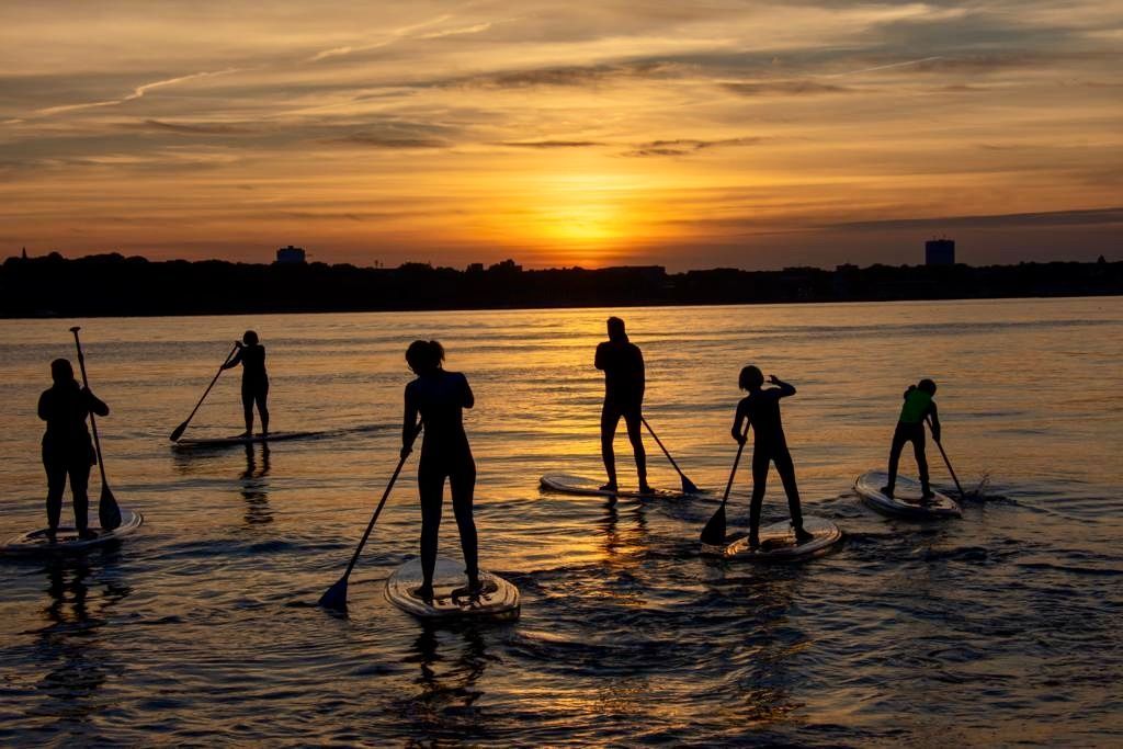 Eine Gruppe von Menschen steht bei Sonnenuntergang auf glassSUPs im Wasser.