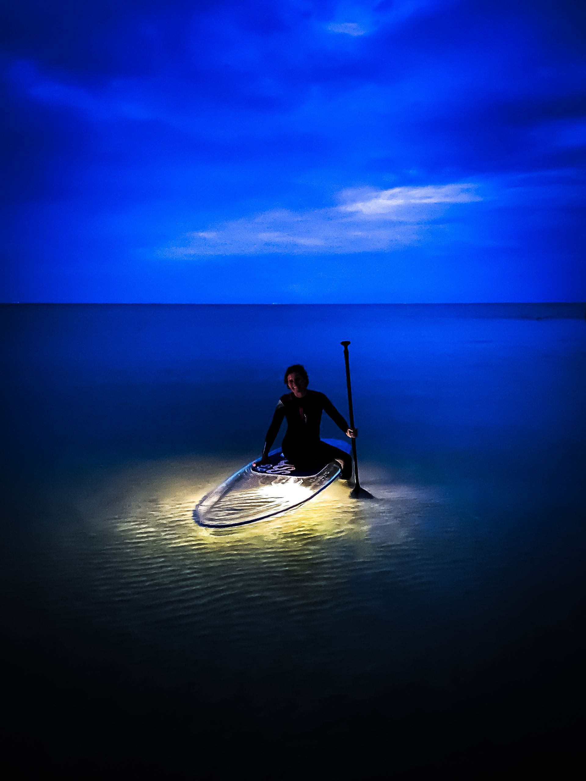 Eine Frau sitzt nachts auf einem beleuchteten glassSUP im Meer