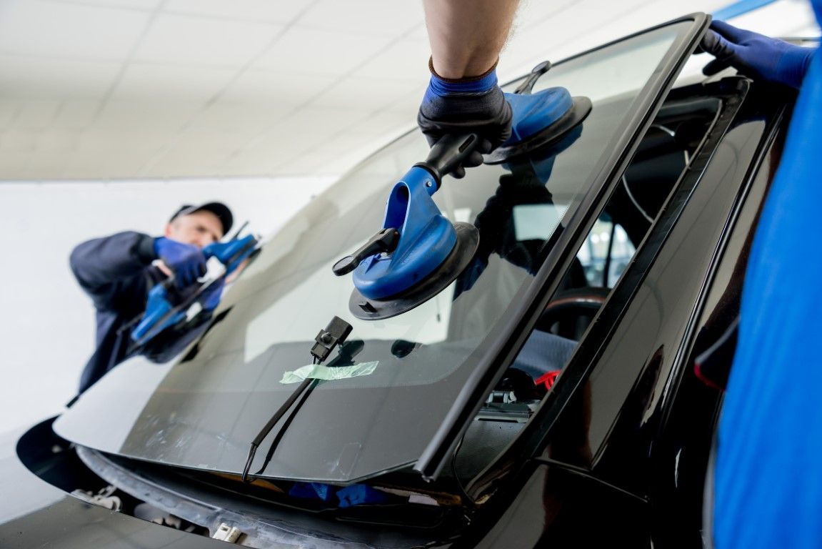 Workers in blue uniforms cleaning a car windshield with blue cloths in a garage